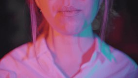 Close-up portrait of young playful girl chewing gum and blowing bubble. Teenager standing in violet spotlight in dark studio carefree posing as part of music video. Concept of youth, model, art.