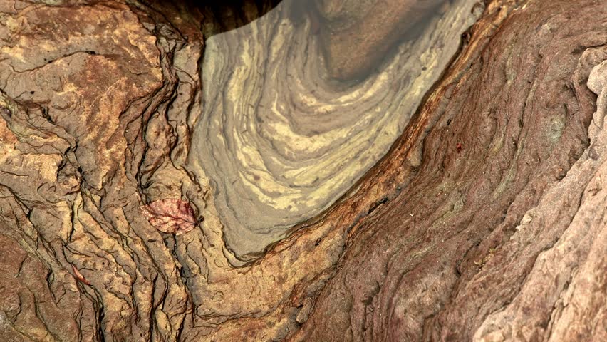 Hand-held shot of erosion layers on a rock with a small water pool