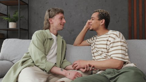Young happy couple two gay men wear casual clothes sits on sofa talk speak couch stay at home hotel flat rest relax spend free spare time in living room indoor. Pride day june month love lgbtq concept Video de stock
