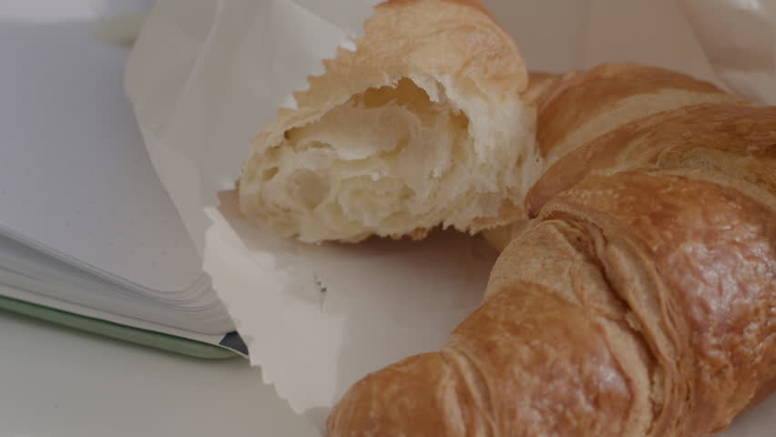 Closeup camera moving to  french croissant  in paper with open book on white chair.
 | Shutterstock HD Video #1103326137
