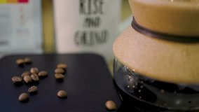 slow motion footage of coffee beans falling into the scene next to a cup of coffee in a beaker and coffee mug. the beans are flying everywhere related to morning, hustle and beverages