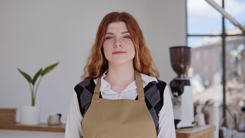 Professional young woman with white healthy smile waitress in apron folding hands, pose at workplace look at camera. Hospitality good customer services, small restaurant owner, cafe staff portrait. Royalty-Free Stock Footage #1103328273