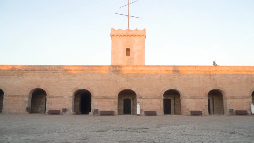 Empty inner courtyard in stone of Montjuic castle wall in Barcelona Spain during sunset with clear blue skies; relaxed leisure; wide forward gimbal shot in 4k; castle fortress tower