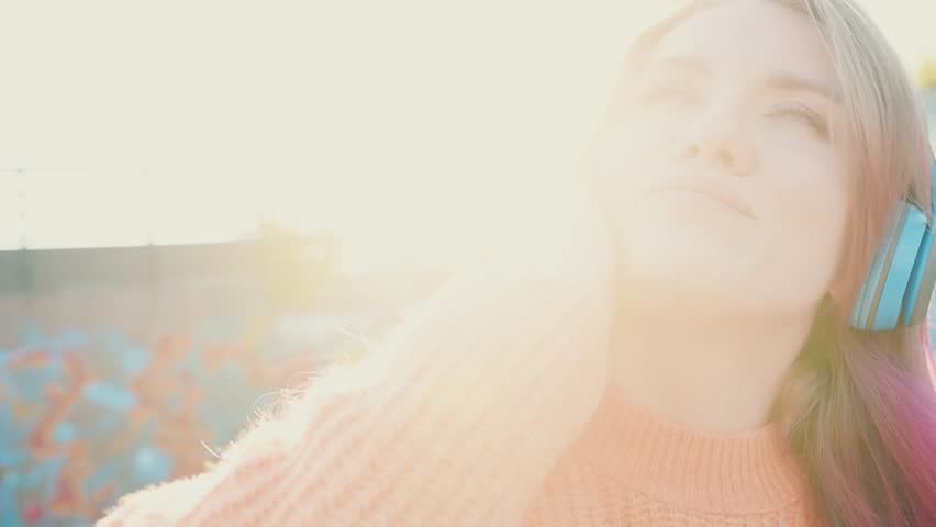 Portrait of a young laughing girl with braces listening to music in headphones in the summer on the street