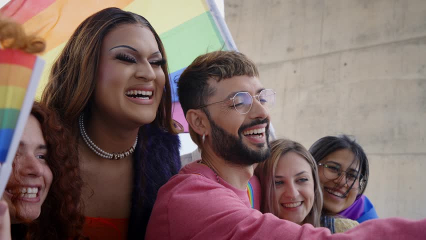 Diverse group of happy young people taking funny selfie for social media celebrating gay pride festival day. Lgbt community concept cheerful friends outdoors. Generation z enjoy party.