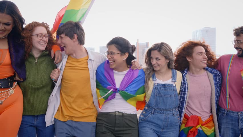Group of young cheerful friends strolling together on day of gay pride parade in city. People LGBT community pose hugging looking smiling at camera outdoor. Generation z and sexual liberation. 