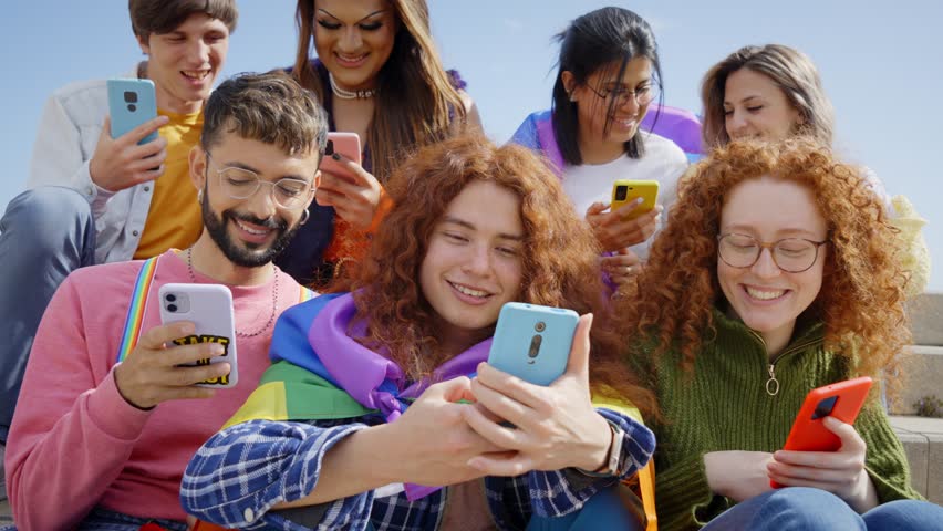 Group young friends watching mobile phone and celebrating gay pride festival day together. Cheerful LGBTIQ community outdoors checking social networks. Lesbian, gay, transgender and non-binary people. Royalty-Free Stock Footage #1103339193