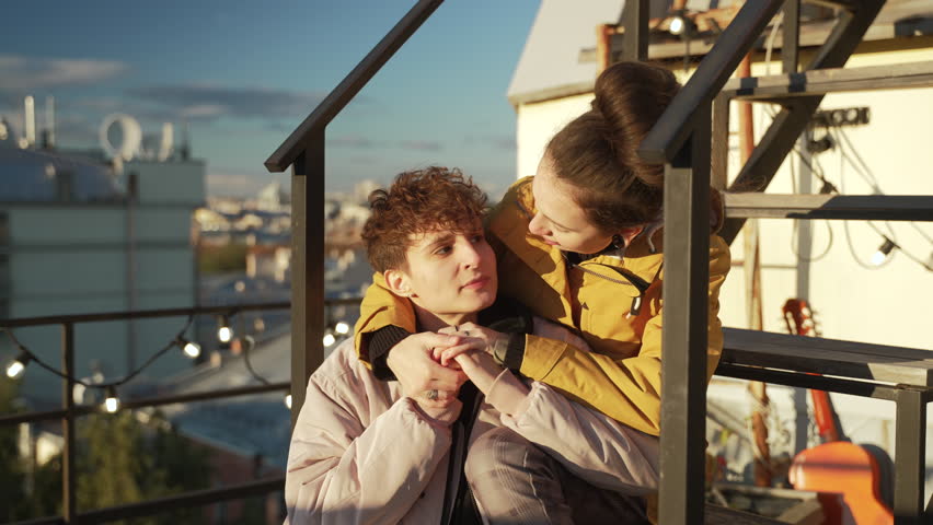 4k Lesbian women talk and hug on rooftop in city spbd. Young lgbt couple talking with happy smiles and hugging tenderly, sitting on roof of building outdoors. Two attractive females pose together and | Shutterstock HD Video #1103341231