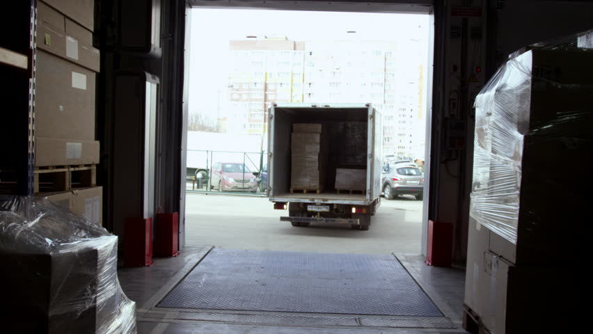 Truck delivers packages to storehouse. Vehicle with cardboard boxes arrives at storehouse open door to unload goods and products Royalty-Free Stock Footage #1103343519
