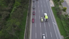 Overhead drone clip following queue of cars and truck moving along fast moving treelined highway with multiple lanes