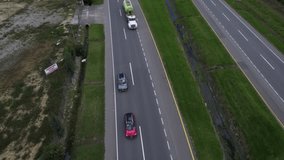 Overhead drone clip over lorry overtaking a queue of cars, moving along a two lane road lines with grass and bushes