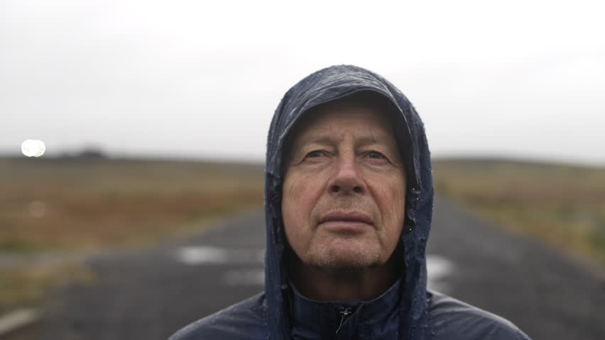 Head shot of a middle-aged man wearing a raincoat hoodie standing in the middle of the road after rainfall