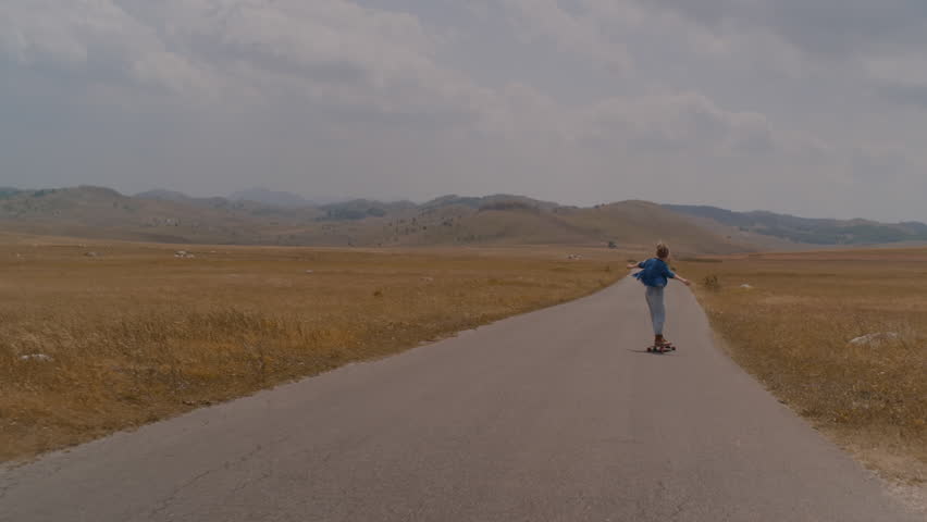 Camera following dreadlocks woman riding on skate longboard  on beautiful mountain view in countryside. 
 | Shutterstock HD Video #1103349393