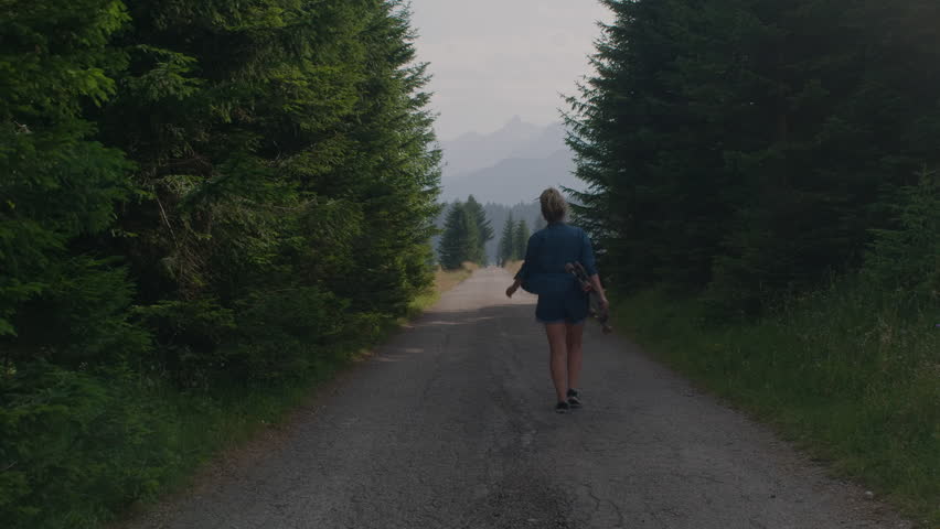 Camera following dreadlocks woman walks with skate longboard on beautiful mountain view in countryside. 
 | Shutterstock HD Video #1103349513