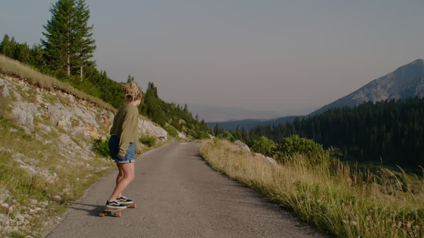 Camera following dreadlocks woman riding on skate longboard  on beautiful mountain view in countryside. Montenegro
