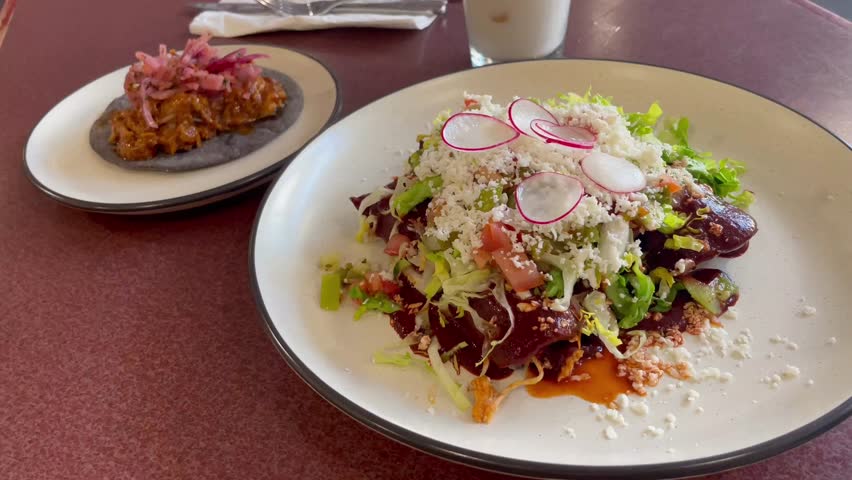 San Francisco, California, United States ; 05,02,2023 : Dish of Chicken Enchiladas with lettuce and cheese with a taco of cochinita pibil