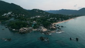 Drone video of the stone shore of tropical beach, drone flies over the blue sea water in the evening before sunset. Seashore of tropical rocky beach on exotic mountain island, dynamic drone footage