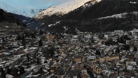 Aerial video of a snowy town in the Tyrol region of Italy during sunset, with towering mountains in the background