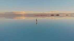 Aerial of a lone figure walking along the mirrored reflection of the world's largest salt flat in Uyuni Salt Flats (Salar de Uyuni), Bolivia. Drone tracking pan shot - Powered by Shutterstock - Get 15% off with code: PIKWIZARD15