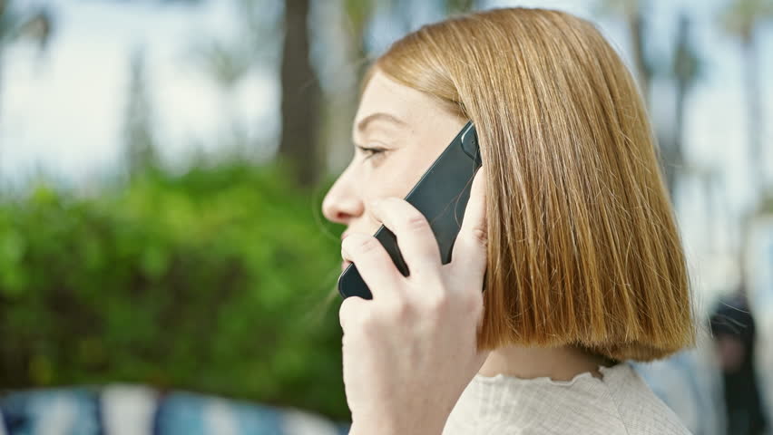 Young blonde woman talking on smartphone at park