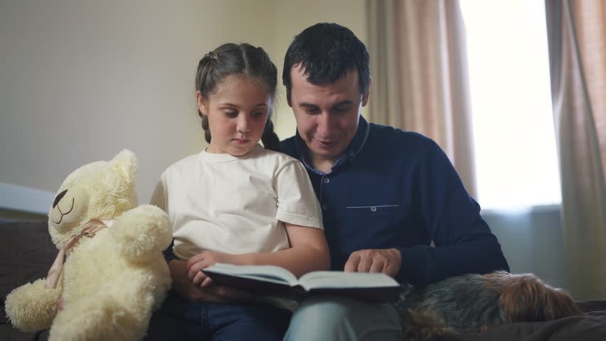 dad reading book to daughter in bedroom. happy family kid dream concept. father parent reads a book at night to his daughter child. dad and lifestyle daughter care and guardianship Royalty-Free Stock Footage #1103379773