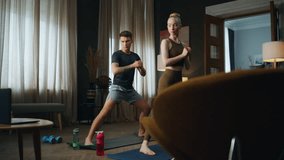 Fit man workouting with slim woman in room watching video lesson. Sporty family couple training body on mat at home. Young guy exercising with blond girl stretching legs. Fitness practice together