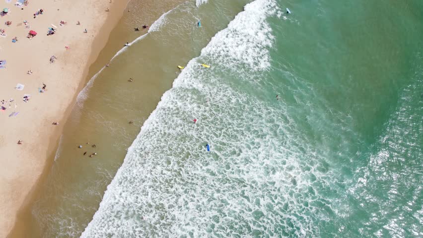 Top view of a beach with surfers practicing in the waves and people sunbathing on the sand. Water sports concept Royalty-Free Stock Footage #1103382981
