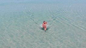 Aerial view of a beautiful woman who is running in the turquoise sea. Top view from drone. 