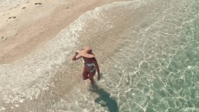 Aerial view of a beautiful woman who is walking along empty beach in the turquoise sea. Top view from drone. 