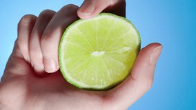 Hand squeezes lime slice and juice flows out on blue background - Powered by Shutterstock - Get 15% off with code: PIKWIZARD15