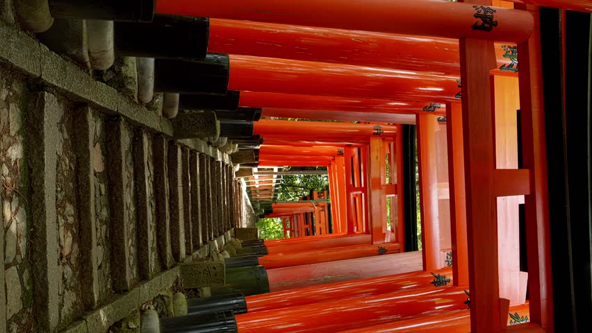 Dramatic view of walking in red gates "Torii", Fushimi Inari Shinto shrine in Kyoto in Japan, Vertical video for smartphone footage, Slow motion, Chinese character in this video means "dedication".
