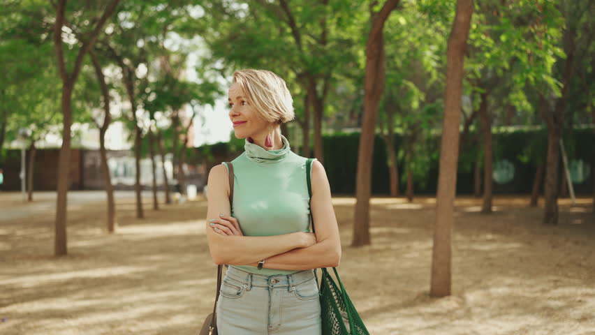 Beautiful smiling woman with short blond hair in casual clothes walks through the city square