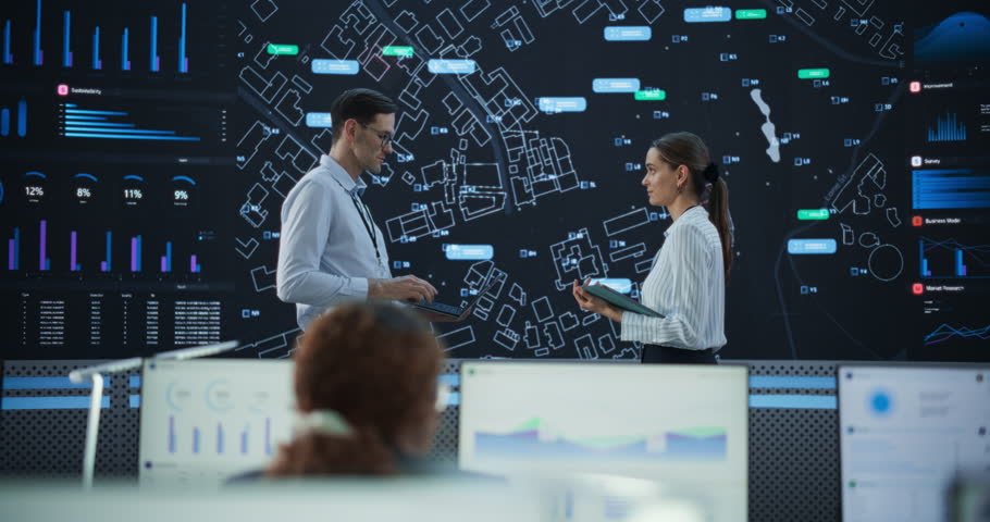 Male And Female Logistics Specialists Discussing New Routs Of Delivery In Front Of Big Digital Screen In Monitoring Office. Diverse Employees Working Behind Desktop Computers For Startup Service. Royalty-Free Stock Footage #1103393047