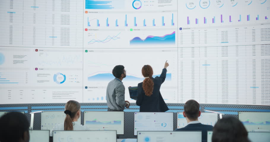 Wide Zoom Out Back Shot Of Diverse Male And Female Risk Managers Analyzing Data On Digital Screen In Monitoring Room. Multiethnic Employees Working On Computers For Succesful Consulting Company