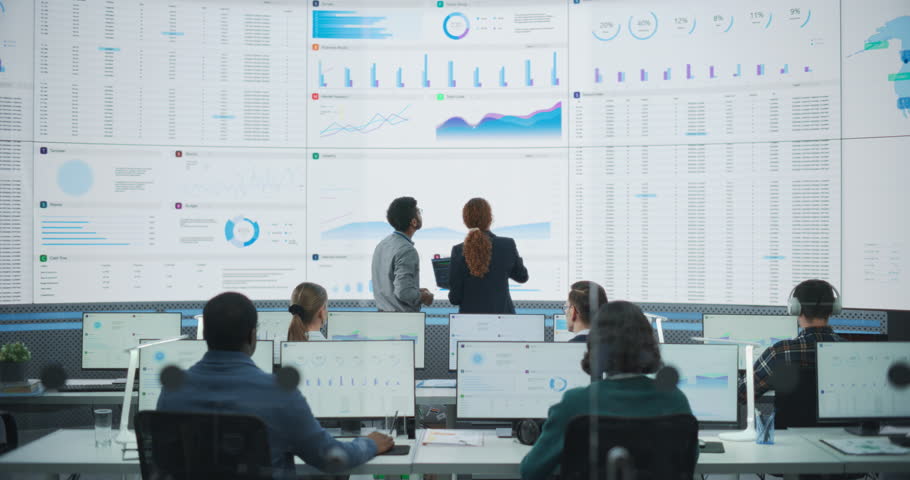 Wide Zoom In Back Shot Of Diverse Male And Female Risk Managers Analyzing Data On Digital Screen In Monitoring Room. Multiethnic Employees Working On Computers For Succesful Venture Capital Company