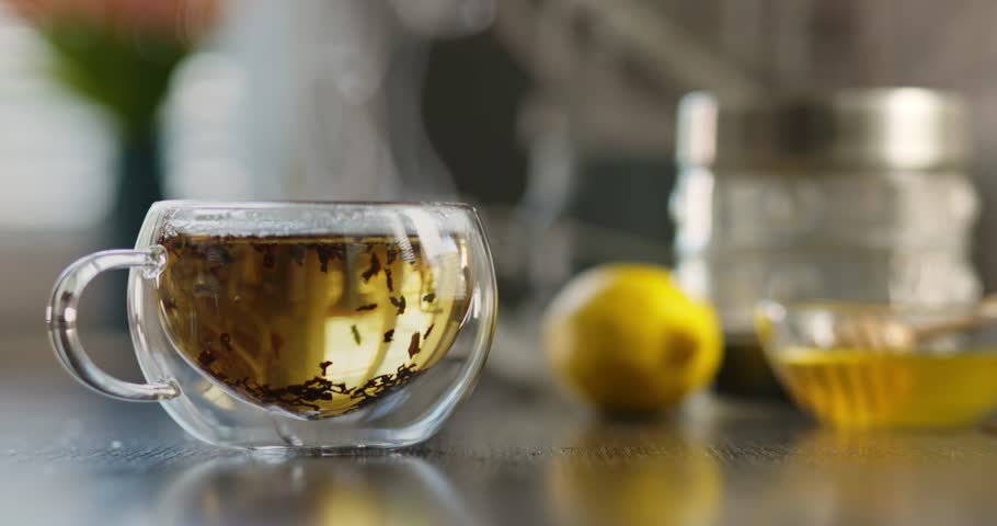  Hot tea in glass cup with smoke on wooden table in kitchen.
