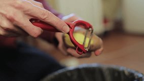 a man peels raw potatoes with a potato peeler in the kitchen, close-up. Close-up of male hands peeling raw potatoes and removing the skin with a potato peeler in slow motion. horizontal video