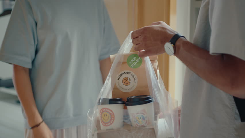 Cropped shot of woman taking plastic bag with food and drinks from delivery guy, closing the door of her apartment Royalty-Free Stock Footage #1103398057
