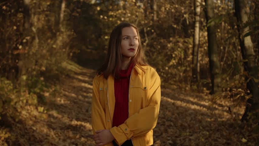 Youg woman walking through autumn forrest with falling leaves