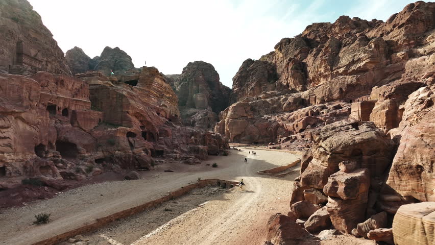 Aerial view following people riding through a desert canyon in Petra, Jordania