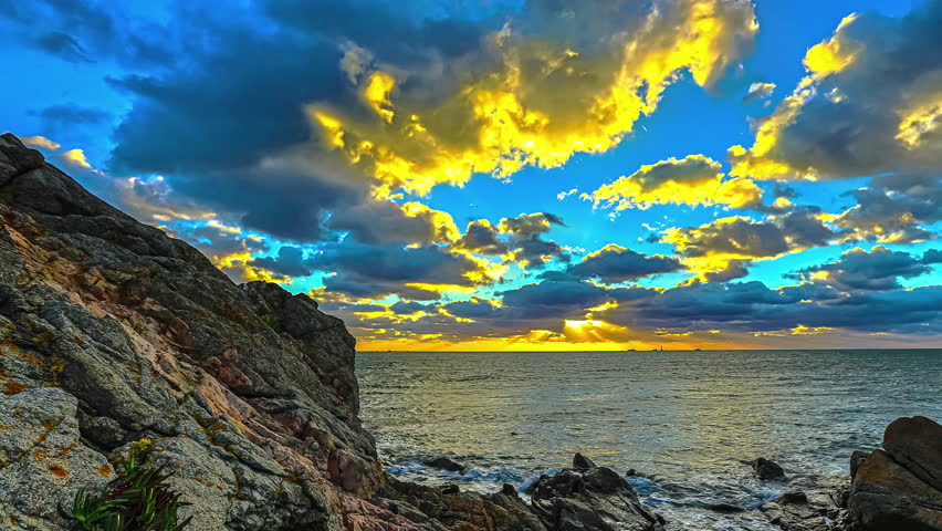 Timelapse of golden sunset sky with moving clouds over ocean and sea rocks