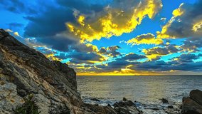 Timelapse of golden sunset sky with moving clouds over ocean and sea rocks