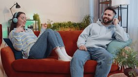 Happy overjoyed young family married couple man woman in wireless headphones dancing on couch at home listening favorite energetic disco rock n roll music. Husband and wife together weekend activities - Powered by Shutterstock - Get 15% off with code: PIKWIZARD15