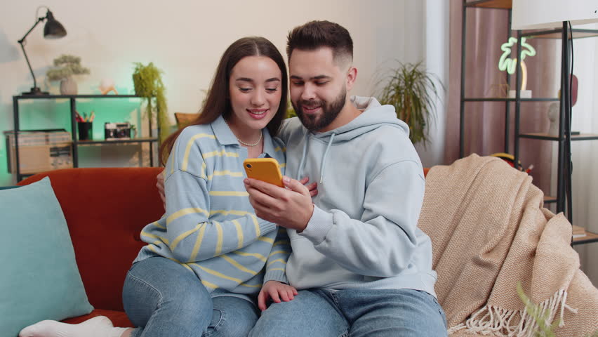 Family couple man woman use mobile smartphone found out great big win good news celebrate lottery jackpot lucky victory, playing game shopping online at home. Husband and wife together on sofa in room Royalty-Free Stock Footage #1103401185