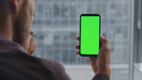 Closeup mockup cellphone in man arms. Unrecognizable attentive startuper holding chroma key mobile analyzing company infographics at home. Anonymous freelancer watching online webinar on green screen - Powered by Shutterstock - Get 15% off with code: PIKWIZARD15