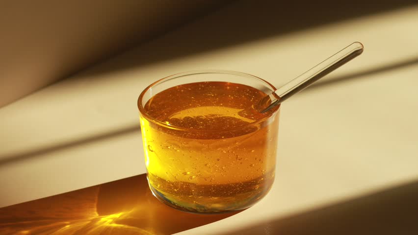 Honey in a transparent jar. A honey spoon is dipped in honey. Honey sparkles in the sun. Royalty-Free Stock Footage #1103409025