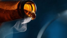 Pouring Beer to Glass - Bottle Tilts and Fog of Gas Comes Out. Stream of Amber Carbonated Liquid Flows in Slow Motion on Dark Blue Background - Powered by Shutterstock - Get 15% off with code: PIKWIZARD15