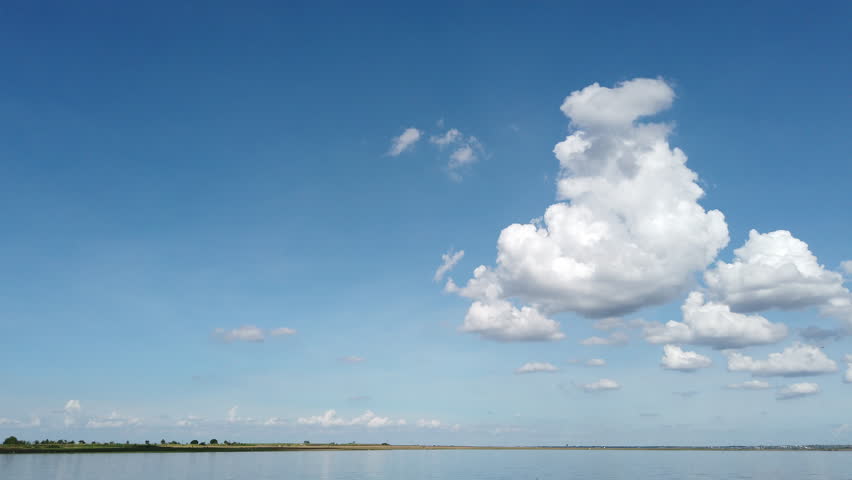Large white monsoon clouds over clear deep blue skies hanging atop a lake in India