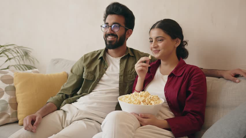 Young happy indian couple watching movie on TV and eating popcorn while relaxing in the living room soft couch  Royalty-Free Stock Footage #1103424767