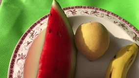 On a plate lies a slice of banana, apple, and watermelon. closeup video 